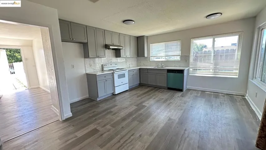 Kitchen with gray cabinetry, white electric range oven, wood finished floors, decorative backsplash, and light countertops