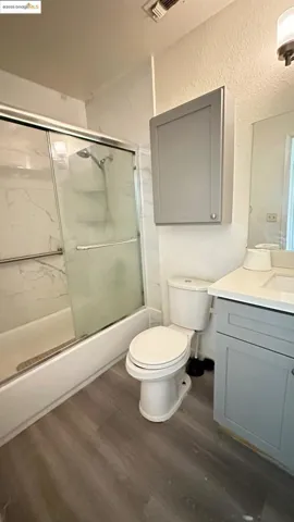 Bathroom featuring wood finished floors, vanity, a textured wall, and enclosed tub / shower combo