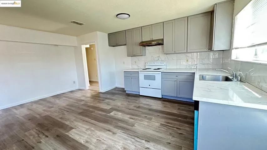 Kitchen with white electric stove, dark wood-style flooring, backsplash, and gray cabinetry