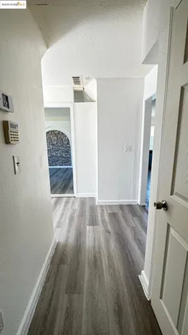 Corridor featuring a textured wall, wood finished floors, arched walkways, and a textured ceiling