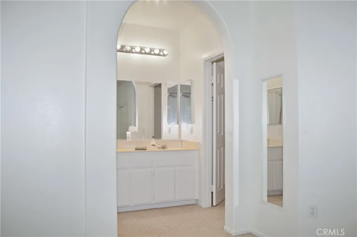 Primary Bedroom Suite with Arched Entry to Ensuite Bath, Two Closets (One a Walk-in), Ceiling Fan, and Back Patio Views