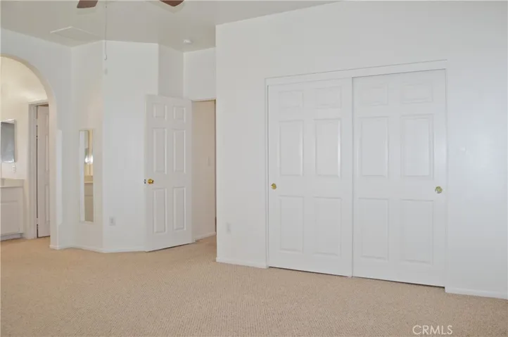 Primary Bedroom Suite with Arched Entry to Ensuite Bath, Two Closets (One a Walk-in), Ceiling Fan, and Back Patio Views