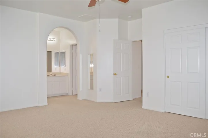 Primary Bedroom Suite with Arched Entry to Ensuite Bath, Two Closets (One a Walk-in), Ceiling Fan, and Back Patio Views