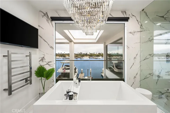 Bathtub overlooking water with tv and towel warming