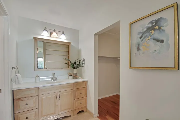 Primary bath features a spacious vanity with ample storage and updated lighting—conveniently located adjacent to a generous walk-in closet with wood flooring.