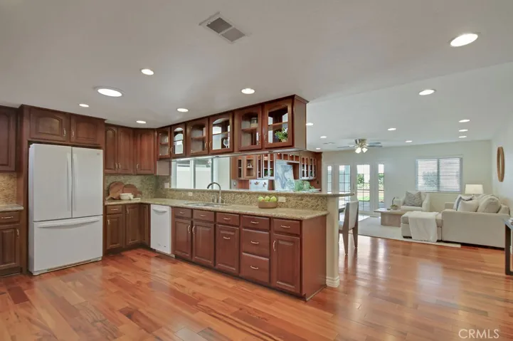 Open-concept kitchen flows seamlessly into the spacious family room—featuring a breakfast bar, wood floors, and French doors that lead to the backyard patio for easy indoor-outdoor living.