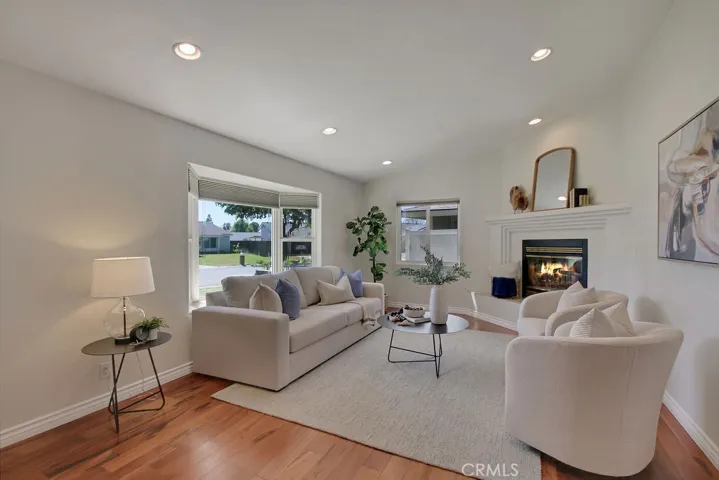 Bright and welcoming living room with recessed lighting, high ceilings, wood floors, a cozy fireplace, and large dual-pane windows that fill the space with natural light.