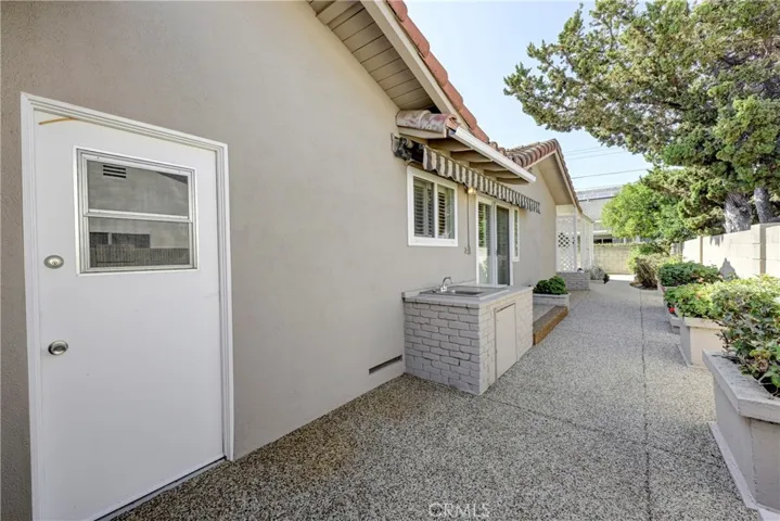 Along the side of the house you see the white door to the garage, a sink area and the slider to the kitchen with an awning.