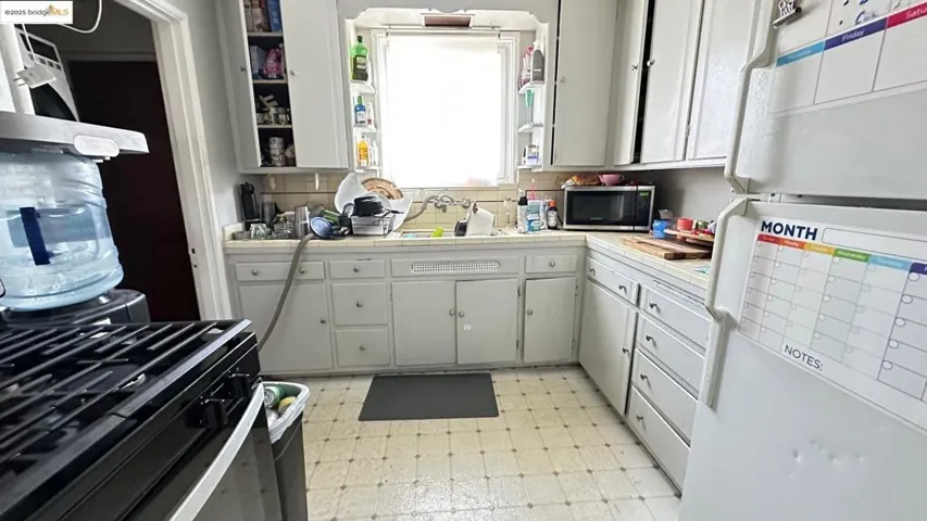 Kitchen featuring freestanding refrigerator, tile countertops, light flooring, and white cabinetry