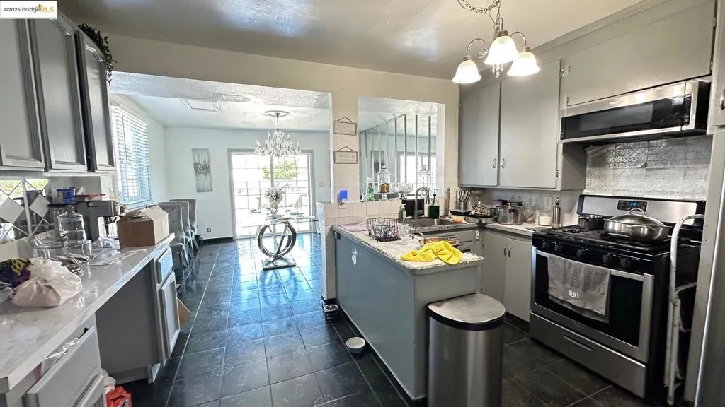 Kitchen featuring backsplash, stainless steel appliances, a chandelier, decorative light fixtures, and light countertops