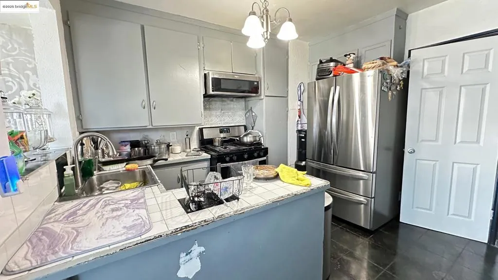Kitchen with stainless steel appliances, gray cabinetry, pendant lighting, tasteful backsplash, and tile counters