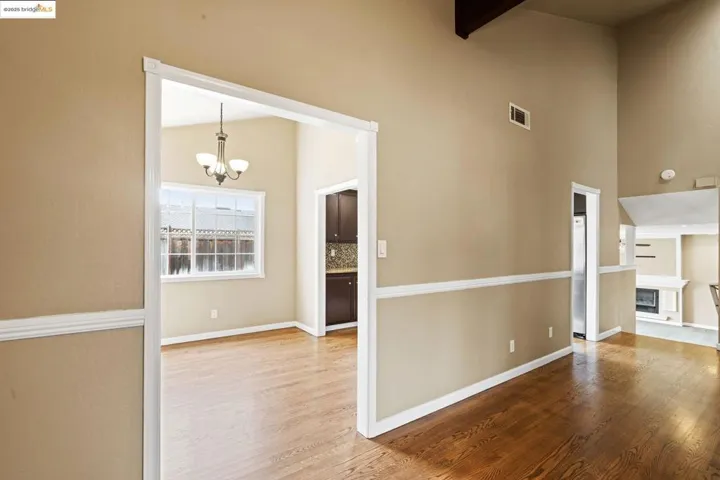 Unfurnished room featuring a chandelier, wood finished floors, beam ceiling, a towering ceiling, and a glass covered fireplace
