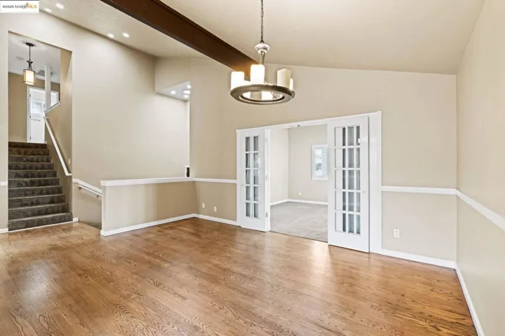 Unfurnished room with french doors, wood finished floors, a chandelier, beam ceiling, and stairway