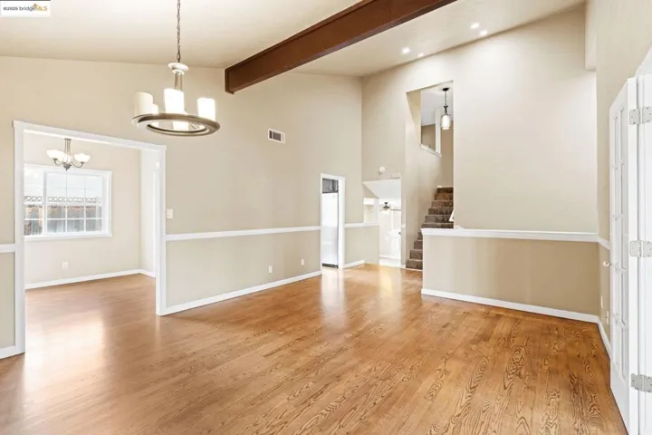 Spare room featuring a chandelier, light wood-style flooring, beam ceiling, stairway, and high vaulted ceiling