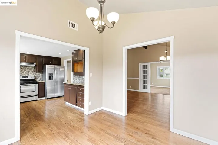Kitchen with a chandelier, dark brown cabinetry, stainless steel appliances, light wood-type flooring, and decorative backsplash