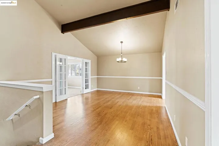 Empty room with beamed ceiling, light wood-style floors, a chandelier, french doors, and high vaulted ceiling