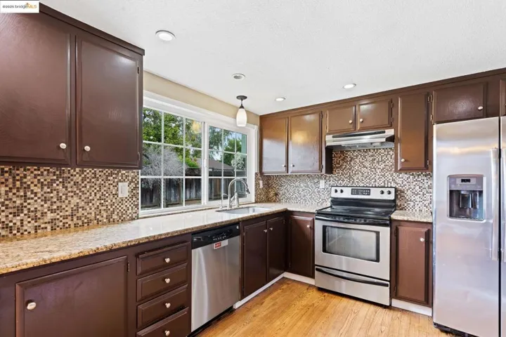 Kitchen with stainless steel appliances, light wood-style flooring, dark brown cabinetry, light stone counters, and recessed lighting