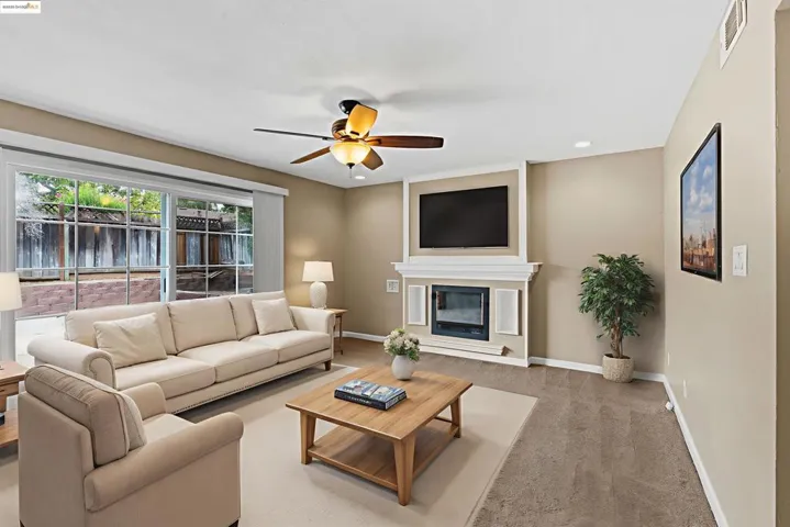 Living room with a glass covered fireplace, carpet flooring, and a ceiling fan