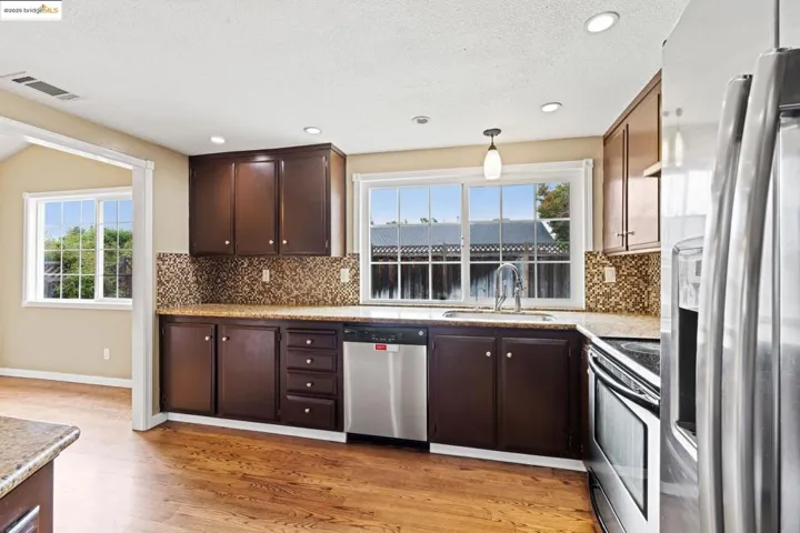 Kitchen featuring appliances with stainless steel finishes, backsplash, light wood-style flooring, a textured ceiling, and dark brown cabinets