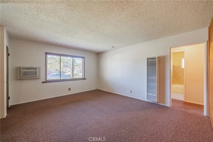 Living room has picture window with view of the front yard, a wall heater and a window AC unit.