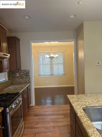 Kitchen featuring stainless steel gas stove, a chandelier, light stone counters, dark wood-style flooring, and recessed lighting