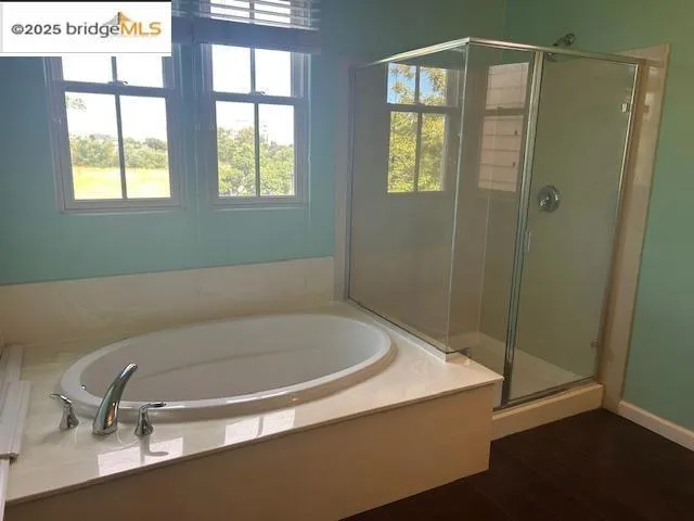 Full bathroom featuring a bath, a stall shower, and wood finished floors