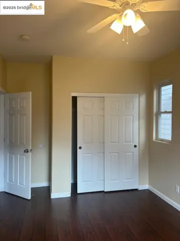Unfurnished bedroom featuring dark wood-style flooring, a closet, and a ceiling fan