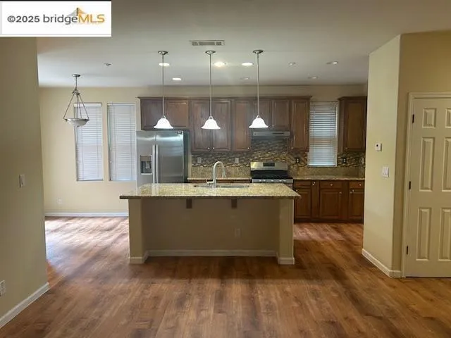 Kitchen featuring appliances with stainless steel finishes, a kitchen breakfast bar, decorative backsplash, dark wood-type flooring, and a center island with sink
