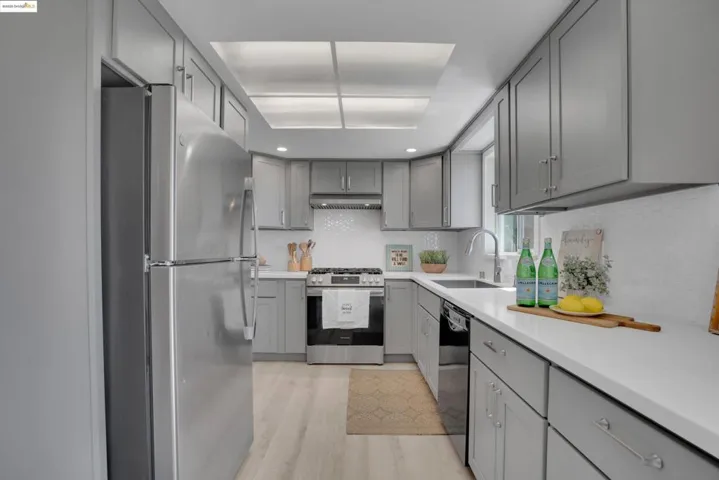 Kitchen with gray cabinetry, appliances with stainless steel finishes, light wood-type flooring, light countertops, and recessed lighting