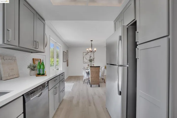 Kitchen featuring gray cabinetry, freestanding refrigerator, a chandelier, dishwashing machine, and light wood-style flooring