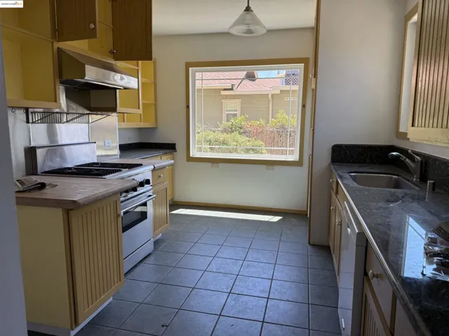 Kitchen with gas range, under cabinet range hood, cream cabinetry, and dishwashing machine