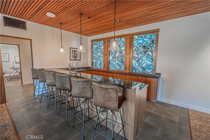 This one-of-a-kind bar showcases a breathtaking backlit geode stone at its entrance, creating a masterpiece you won’t see anywhere else. And not to mention the custom slat ceiling.