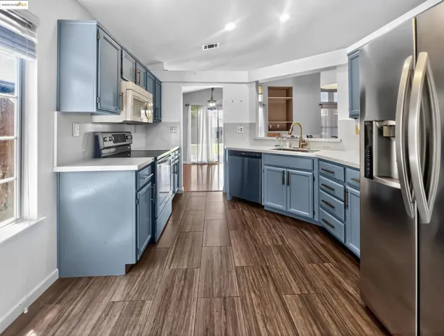 Kitchen featuring blue cabinetry, stainless steel appliances, light countertops, lofted ceiling, and dark wood-style floors