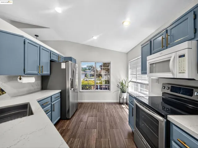 Kitchen featuring stainless steel appliances, blue cabinets, vaulted ceiling, dark wood-style flooring, and recessed lighting