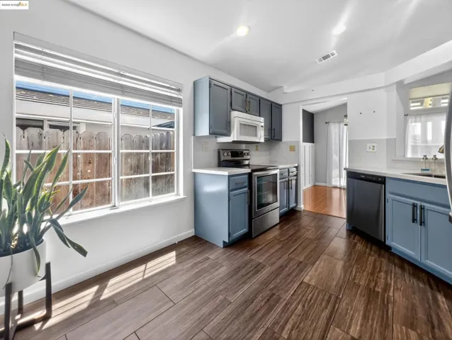 Kitchen with blue cabinetry, appliances with stainless steel finishes, vaulted ceiling, light countertops, and wood finish floors