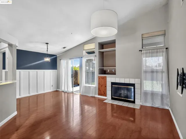 Unfurnished living room with built in features, a fireplace, lofted ceiling, wood finished floors, and wainscoting
