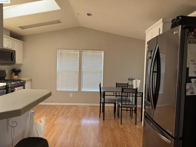 Kitchen featuring stainless steel appliances, vaulted ceiling, white cabinetry, light wood-type flooring, and a kitchen bar