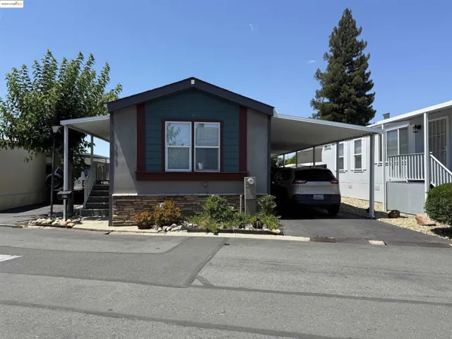 Manufactured / mobile home featuring a carport, concrete driveway, and stairs