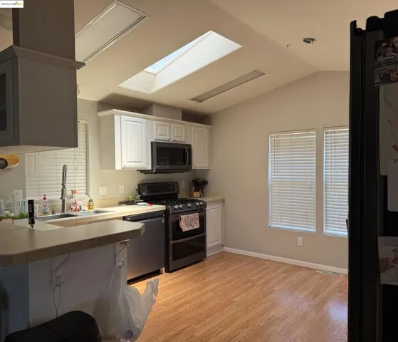 Kitchen with double oven range, vaulted ceiling, light wood-style floors, dishwasher, and white cabinets