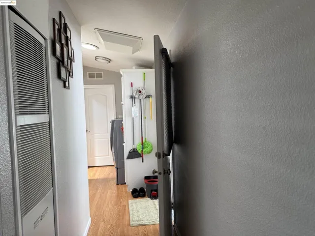 Hall with a heating unit, a textured wall, light wood finished floors, and washer / dryer