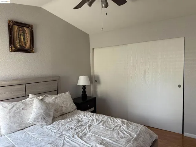 Bedroom with wood finished floors, lofted ceiling, a textured wall, and ceiling fan