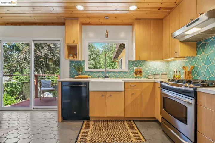 Kitchen featuring gas stove, under cabinet range hood, black dishwasher, light countertops, and decorative backsplash