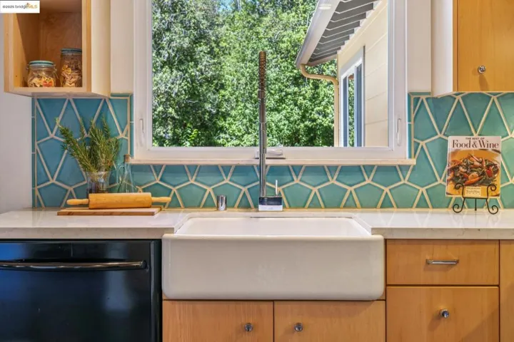 Kitchen with black dishwasher, light stone counters, and backsplash