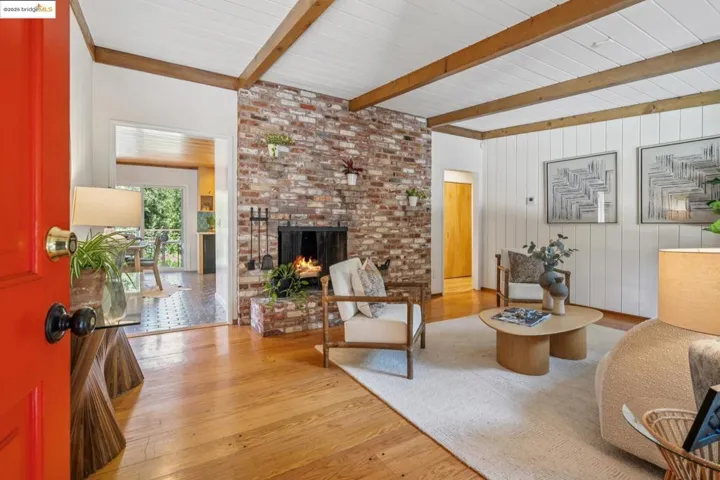 Living room featuring wood-type flooring, a brick fireplace, wood walls, and a wood ceiling with exposed beams