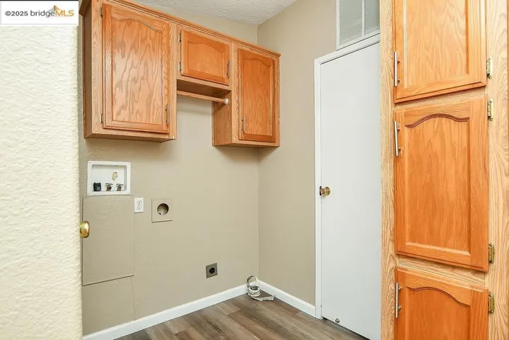 Washroom with hookup for an electric dryer, cabinet space, hookup for a washing machine, and wood finished floors