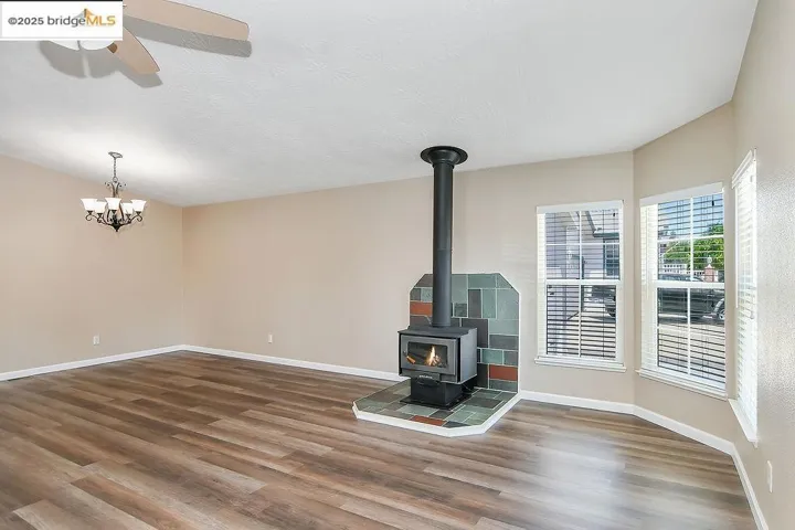 Unfurnished living room featuring wood finished floors, a wood stove, a ceiling fan, a chandelier, and a textured ceiling