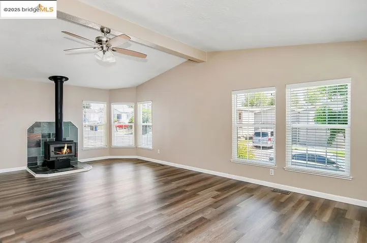 Unfurnished living room with a wood stove, dark wood finished floors, and a ceiling fan