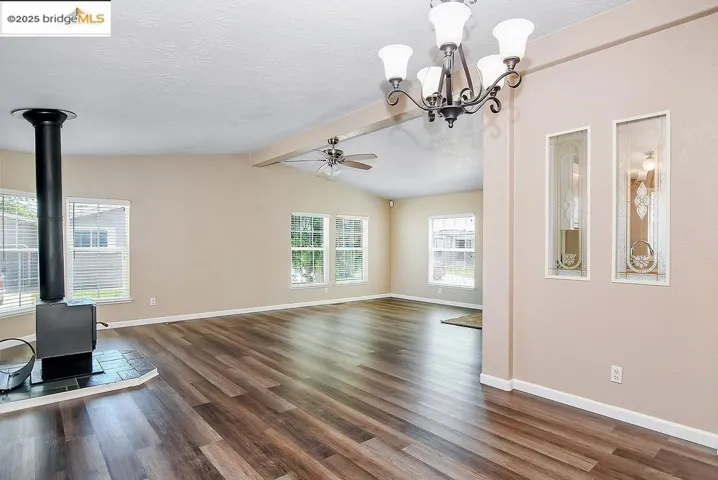 Unfurnished living room with a wood stove, a ceiling fan, dark wood-style flooring, a chandelier, and a textured ceiling