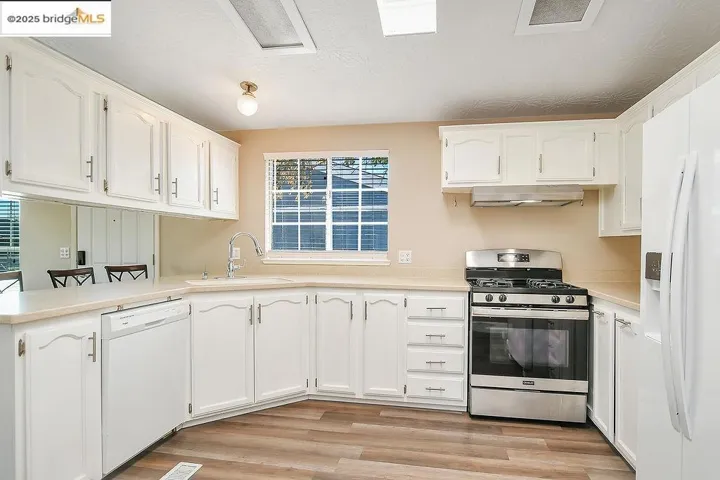Kitchen with white appliances, white cabinetry, light countertops, and light wood-type flooring