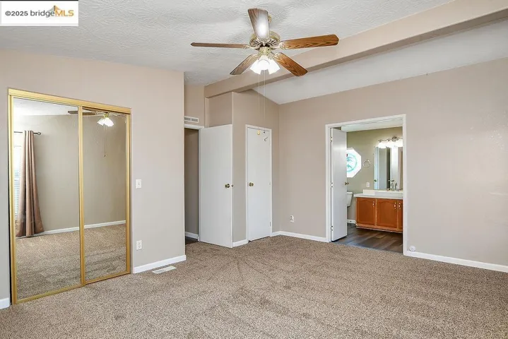 Unfurnished bedroom with carpet flooring, ensuite bathroom, a ceiling fan, and lofted ceiling